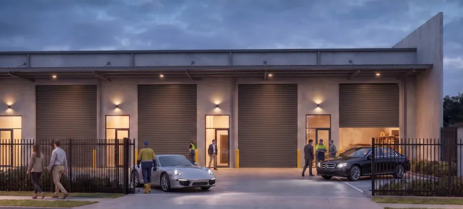 Industrial units at dusk with roller doors lit from within and tenants and vehicles in the forecourt.
