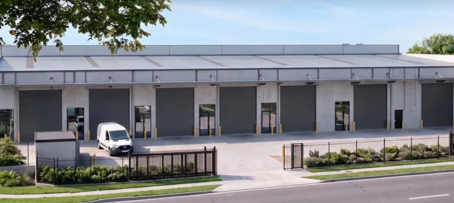 Row of tilt-panel industrial units with roller doors, awnings and hardstand, seen from the street.