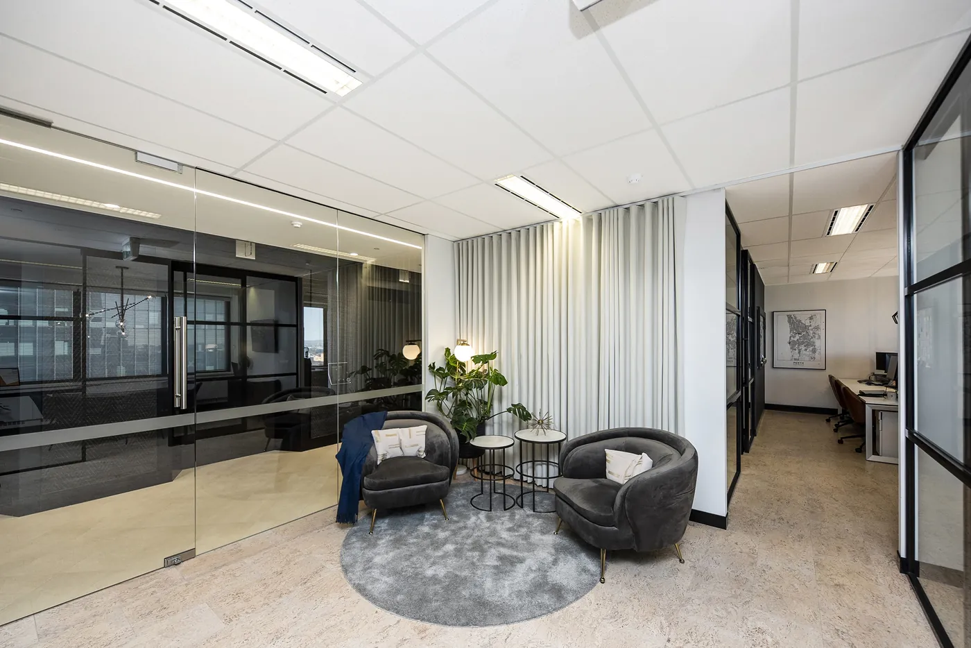 Benchmark — Breakout lounge with black-framed glazed partitions and travertine floor.