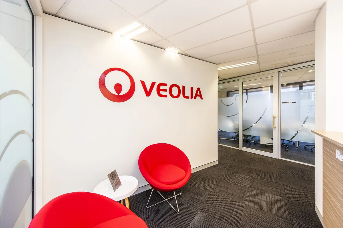 VEOLIA office fitout, Melville Parade South Perth — branded feature wall above red tub chairs in the visitor lounge.